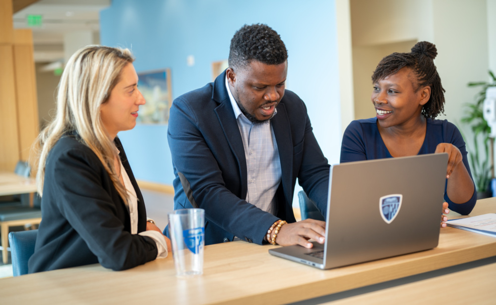 three students sitting at desk looking at laptop