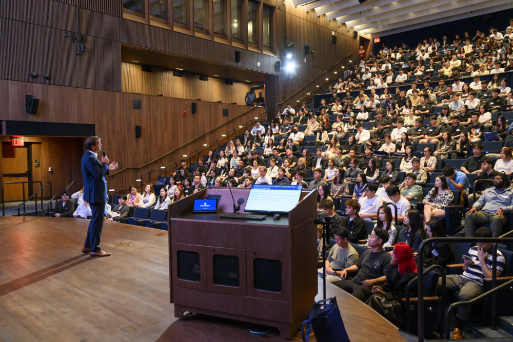 person presenting on a stage in front of an auditorium filled with people