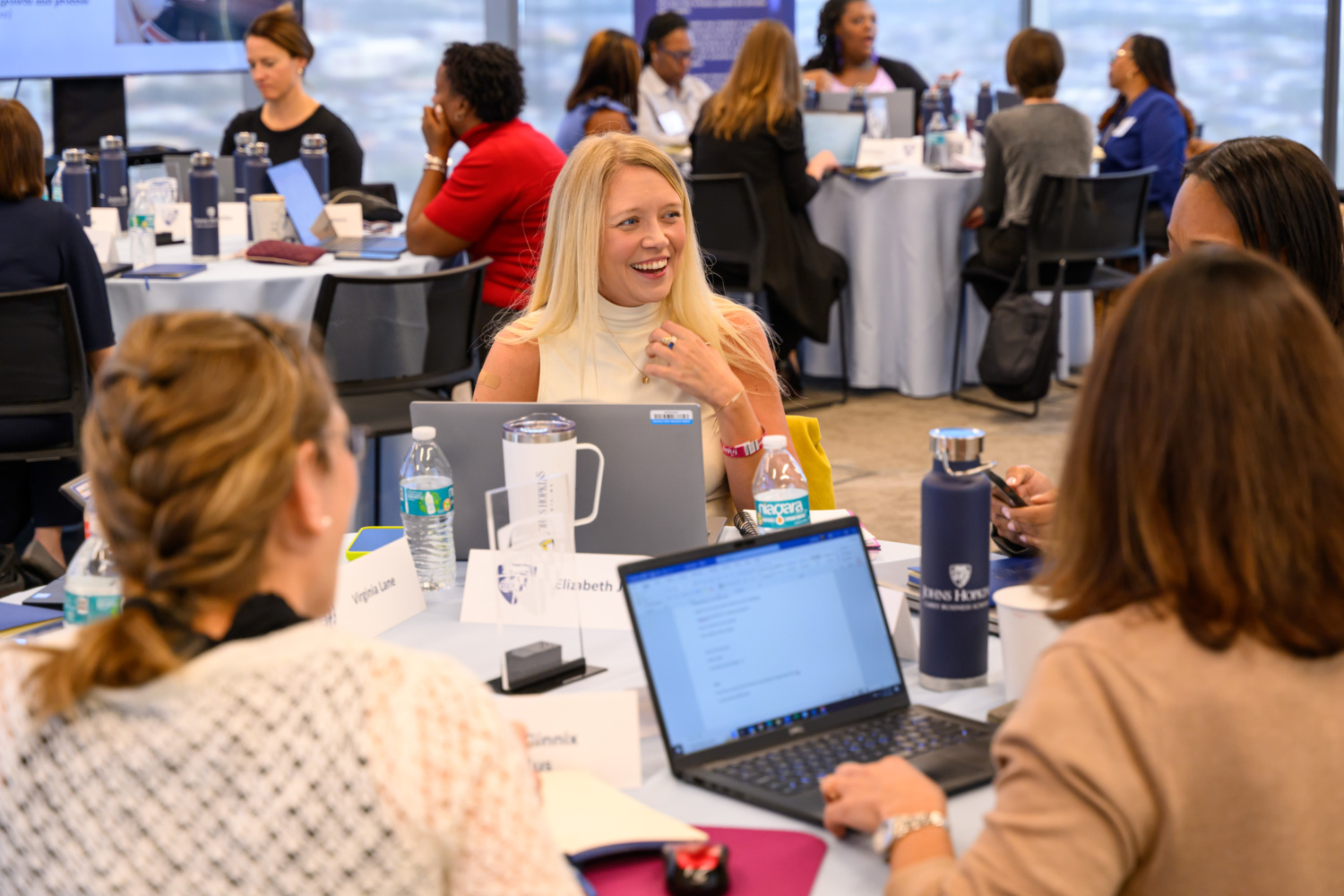 women sitting at a table on their laptops talking to each other