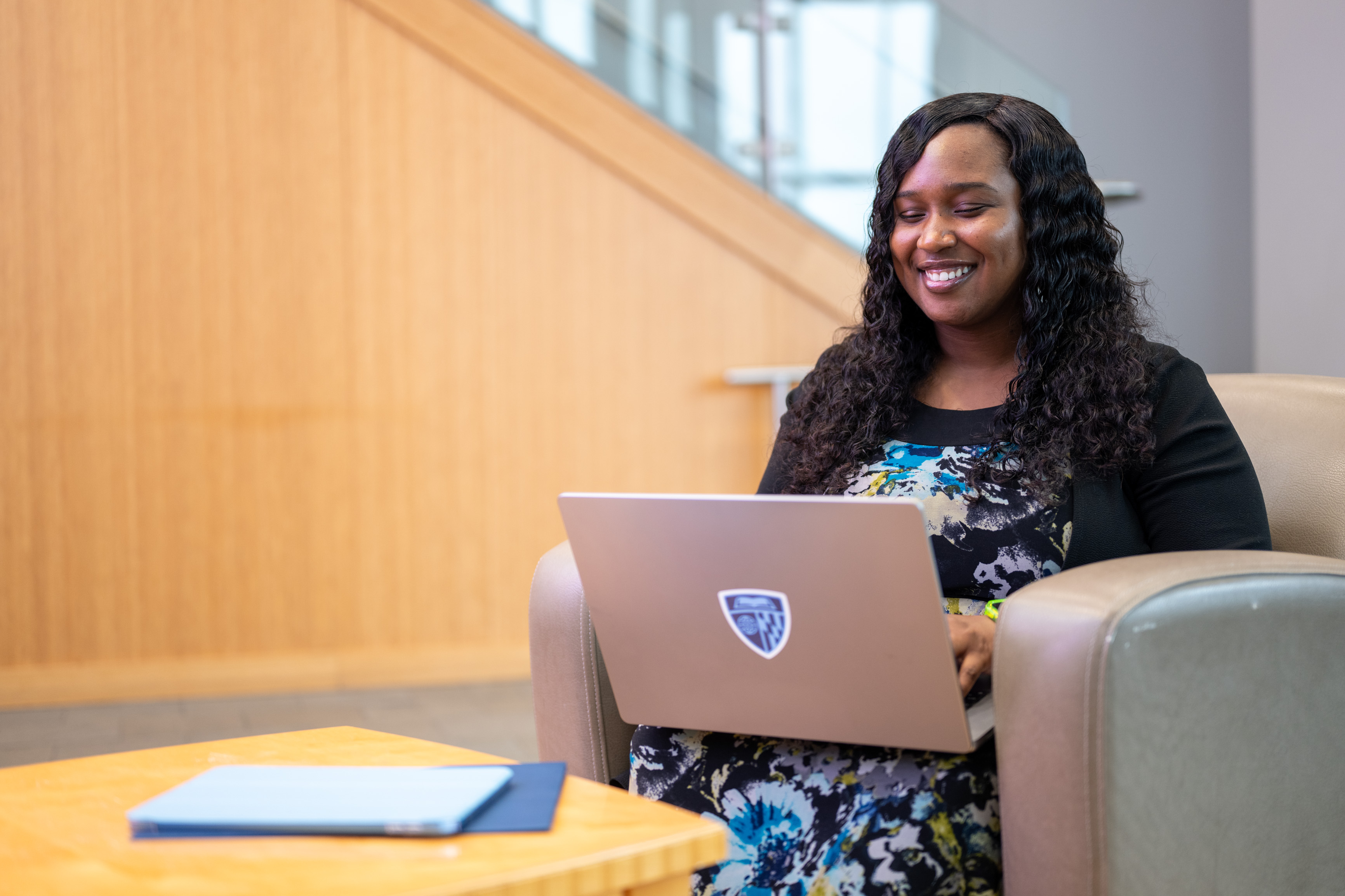 person smiling and sitting in a chair with a laptop open in their lap