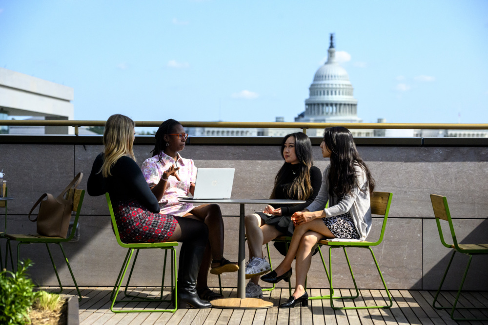 Four people sitting at a table outside with the Capitol building in the background