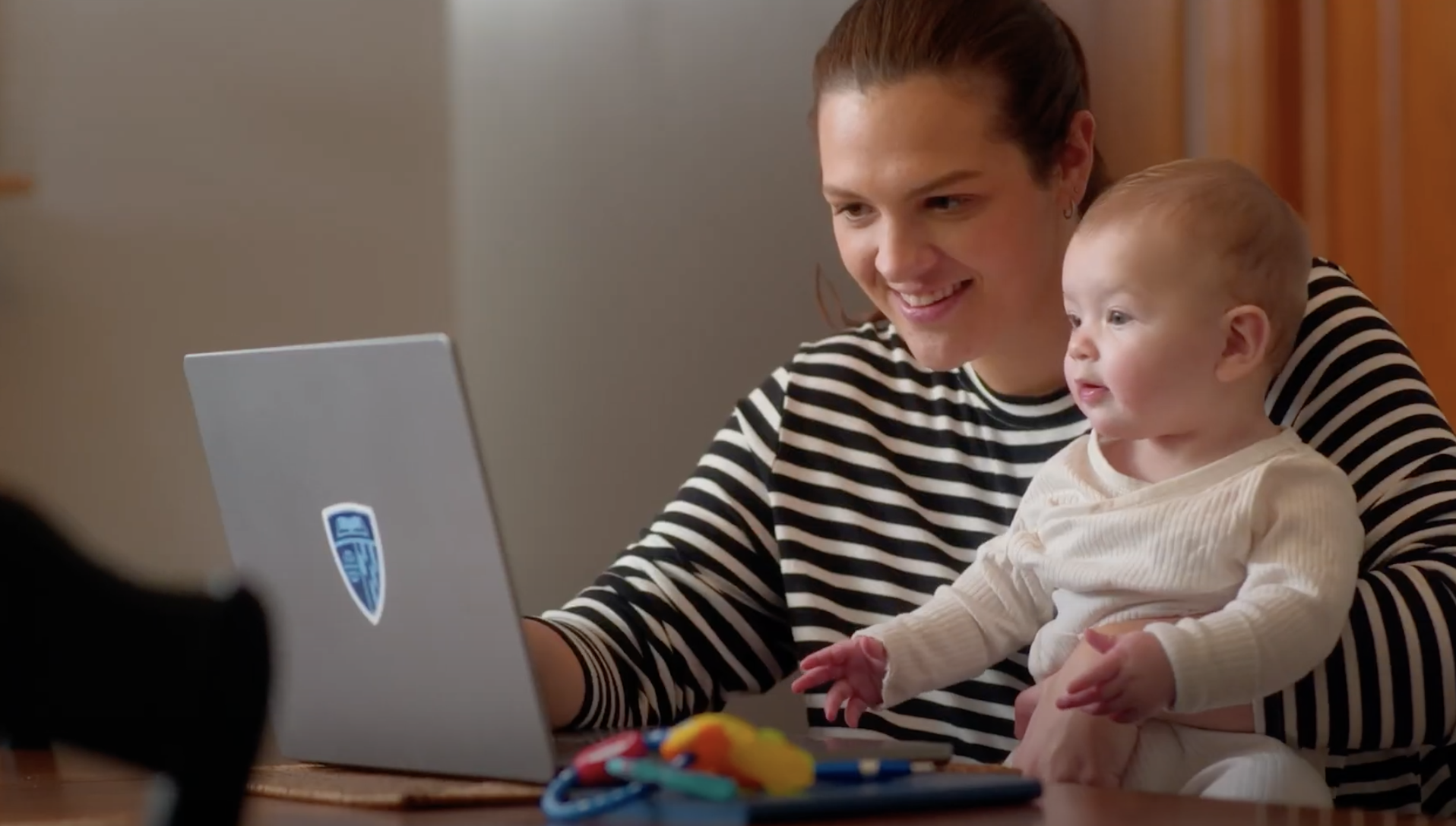 person holding baby in lap at a table with laptop in front of them on table