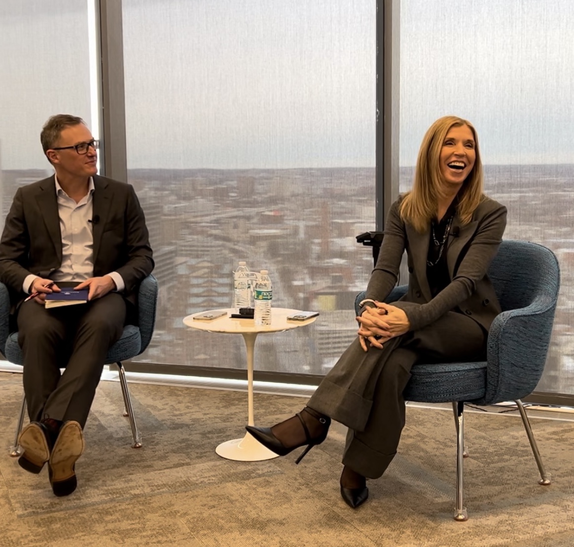 two people sitting in chairs with a small table between them, looking to the side and smiling