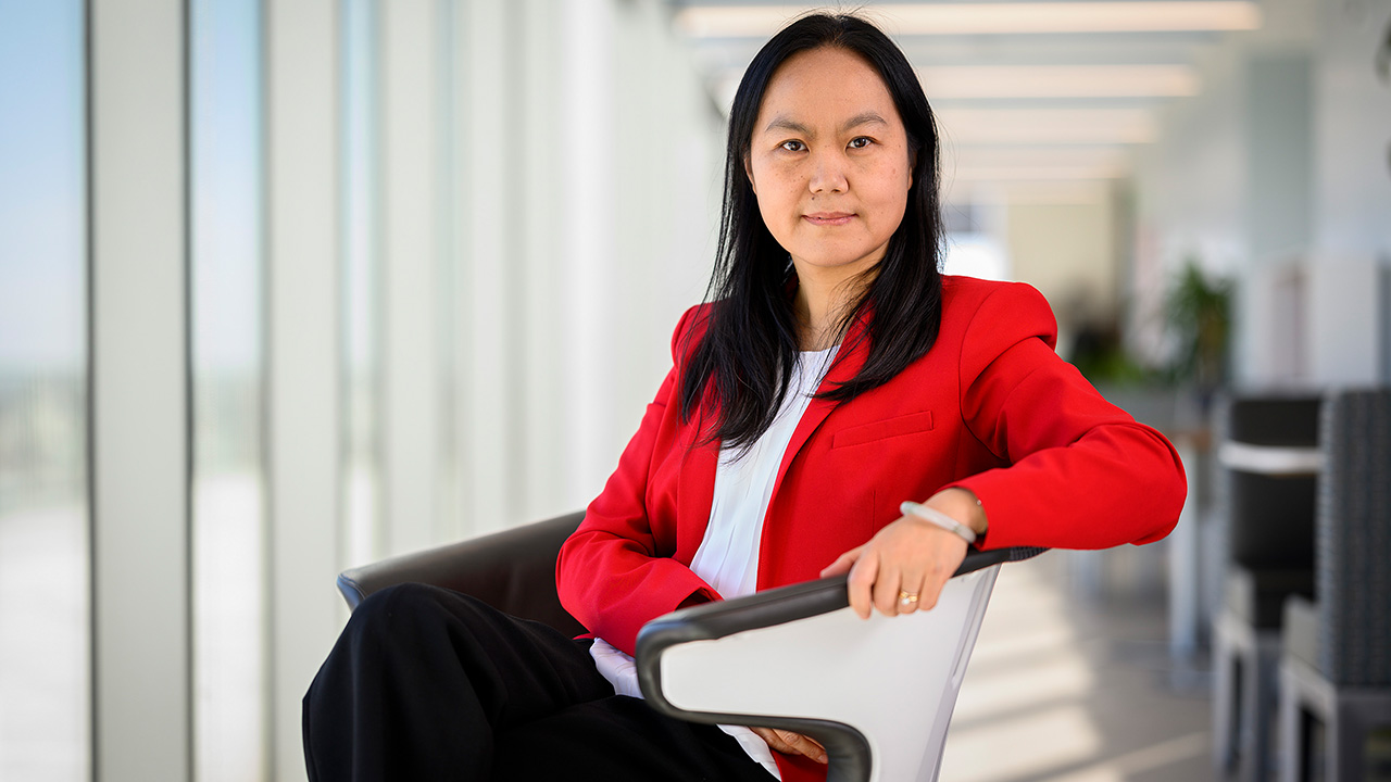 person sitting in chair in front of a window, smiling for photo in business attire