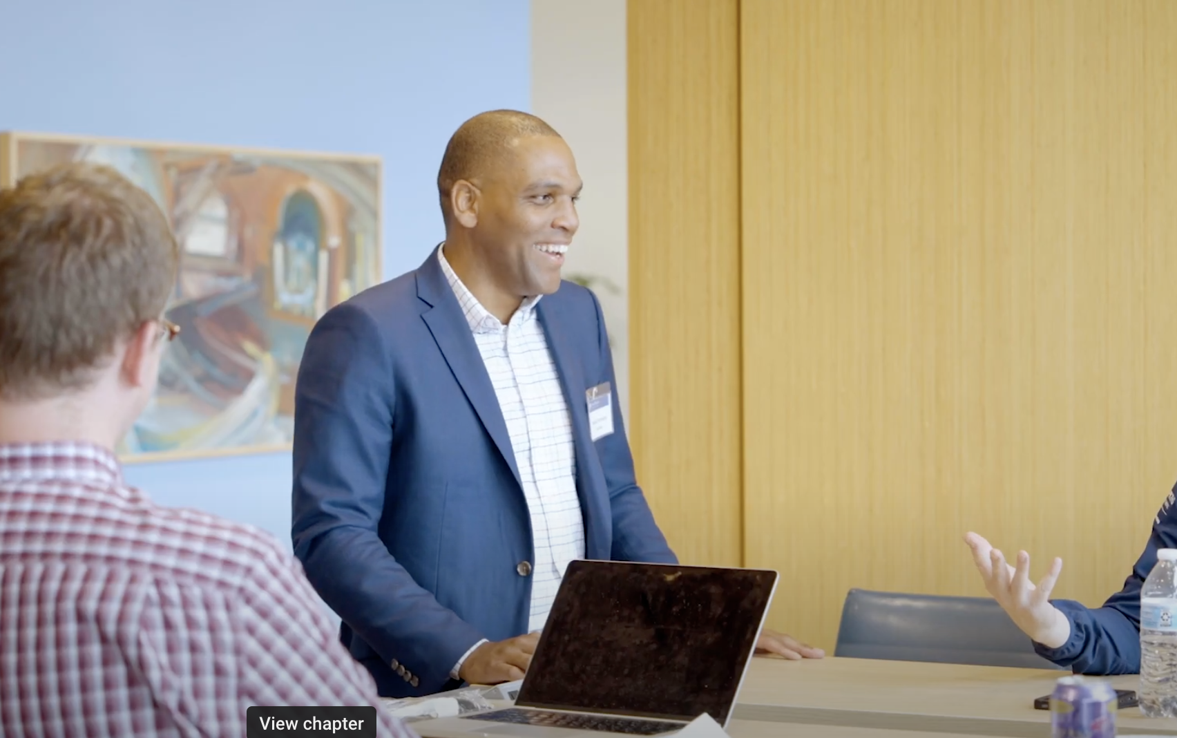 person standing in front of a table with a few laptops out on the table and a person sitting next to them