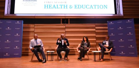 four people sitting on a stage talking with a projector screen in the back of them