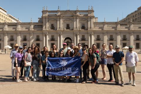 students in front of a building holding the Johns Hopkins Carey Business School flag