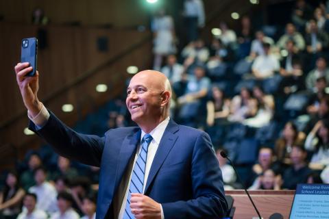 person standing in front of a crowd with a phone held high taking a selfie with the audience behind