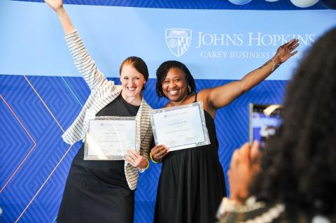 two people smiling for a photo holding certificates with their other hands in the air