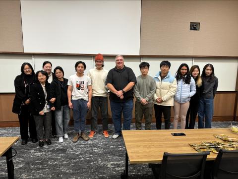 people standing up standing together in a line smiling for a photo in a classroom