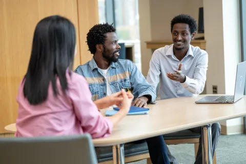 three people sitting at a desk, one is speaking