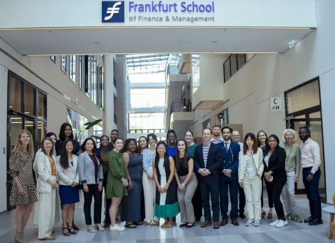 group of people posing for photo inside, standing under a sign that says frankfurt school of finance & mangement