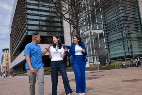 three people walking outside talking to each other on a sidewalk