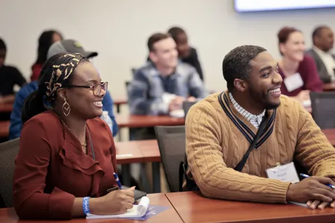 two people sitting at a desk, smiling and looking to the side