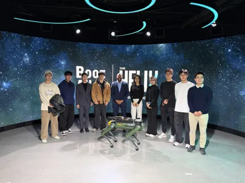 people standing in a row, smiling for photo at booz allen helix center, with a robot in front