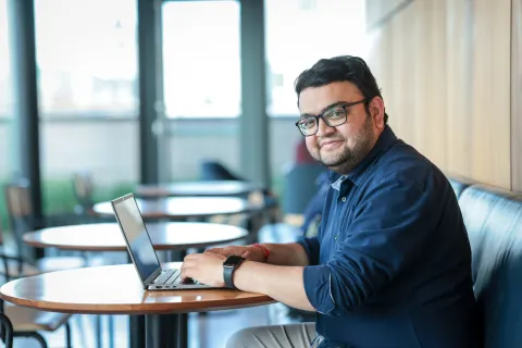 person sitting at table with laptop, looking at camera smiling