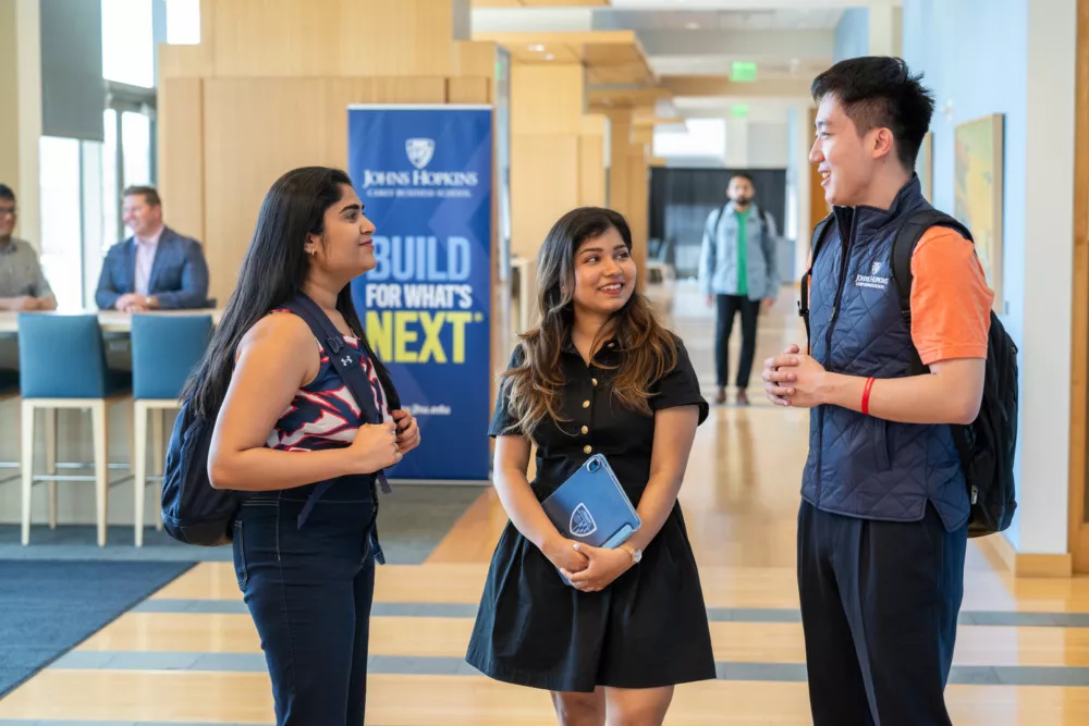 three students standing in a hallway of a school with a build for what's next&amp;quot; banner in the background