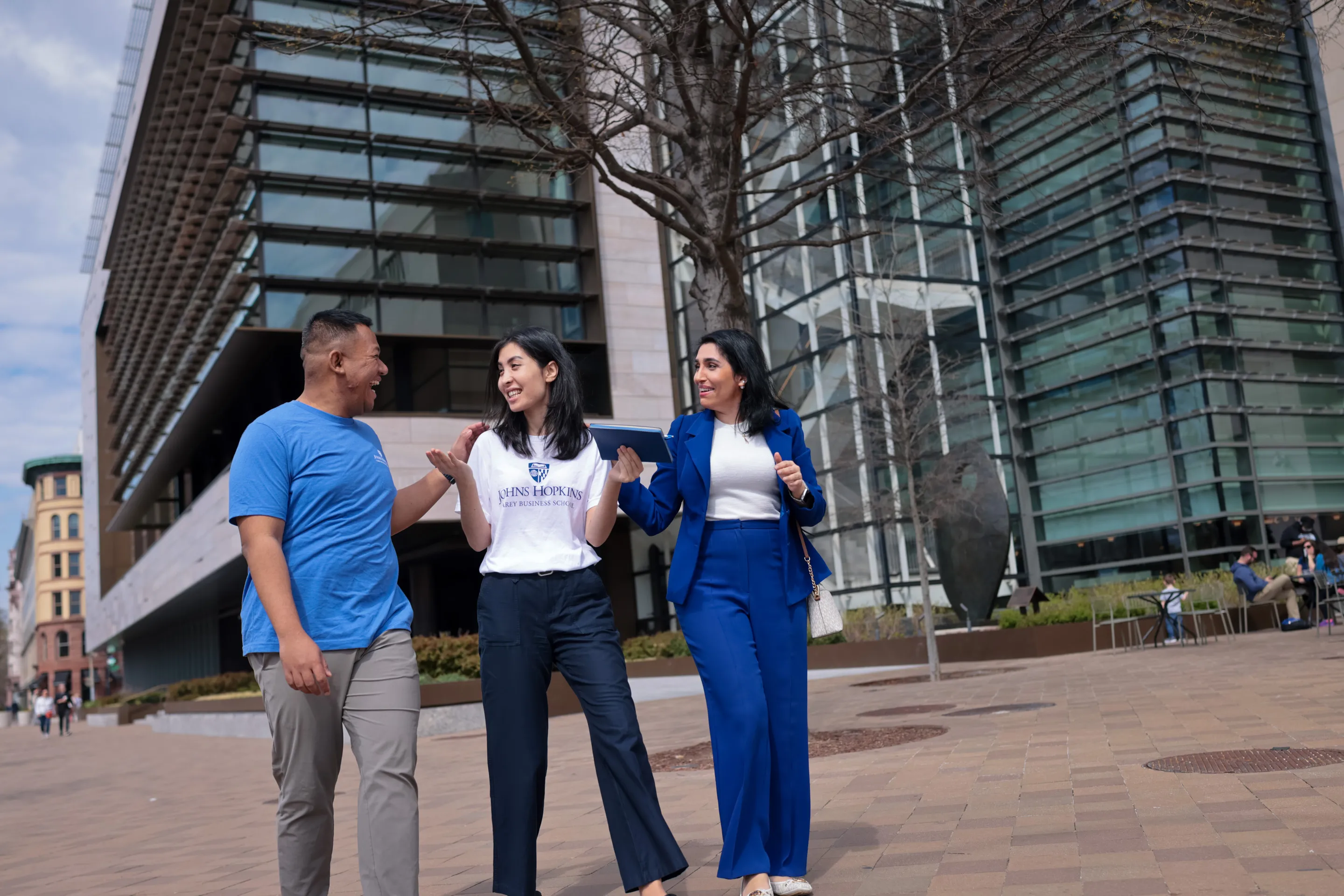 three people walking outside talking to each other on a sidewalk