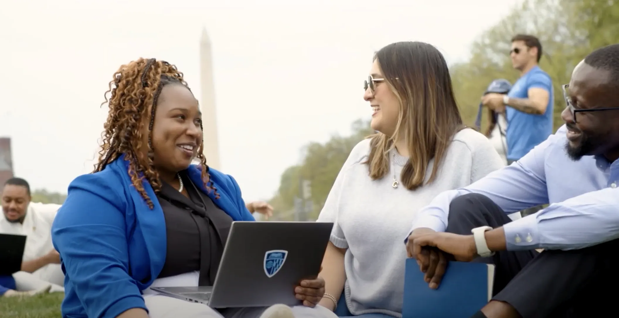three people sitting outside on the grass with the washington monument in the background