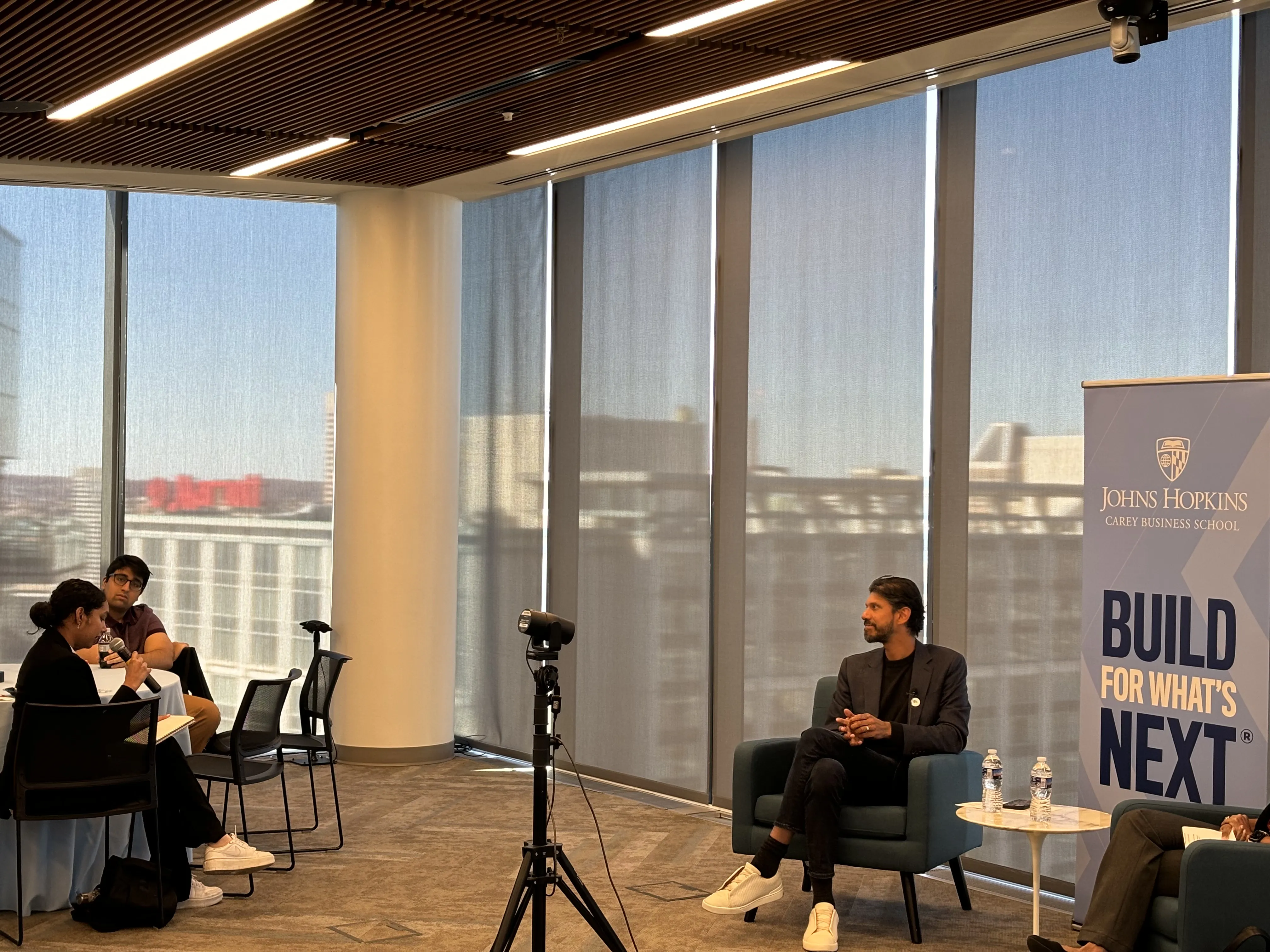 student holding microphone talking into it and person sitting in front of class listening