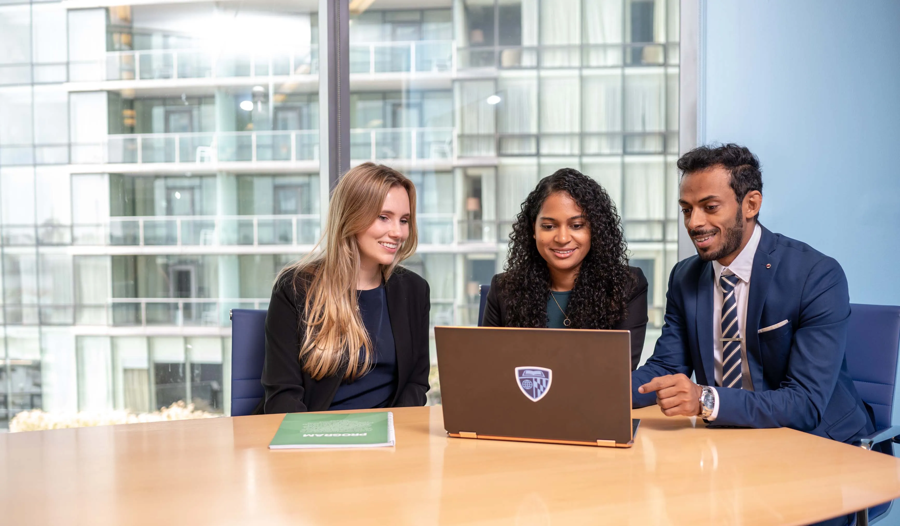 three people sitting at a table, all looking at a laptop screen