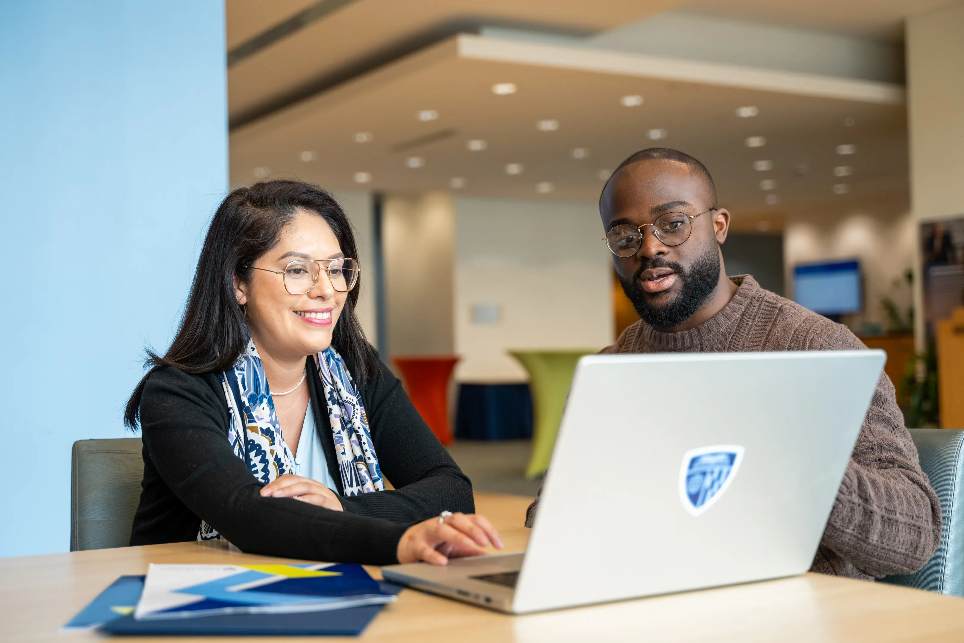 two people sitting at a desk, looking at the same laptop screen