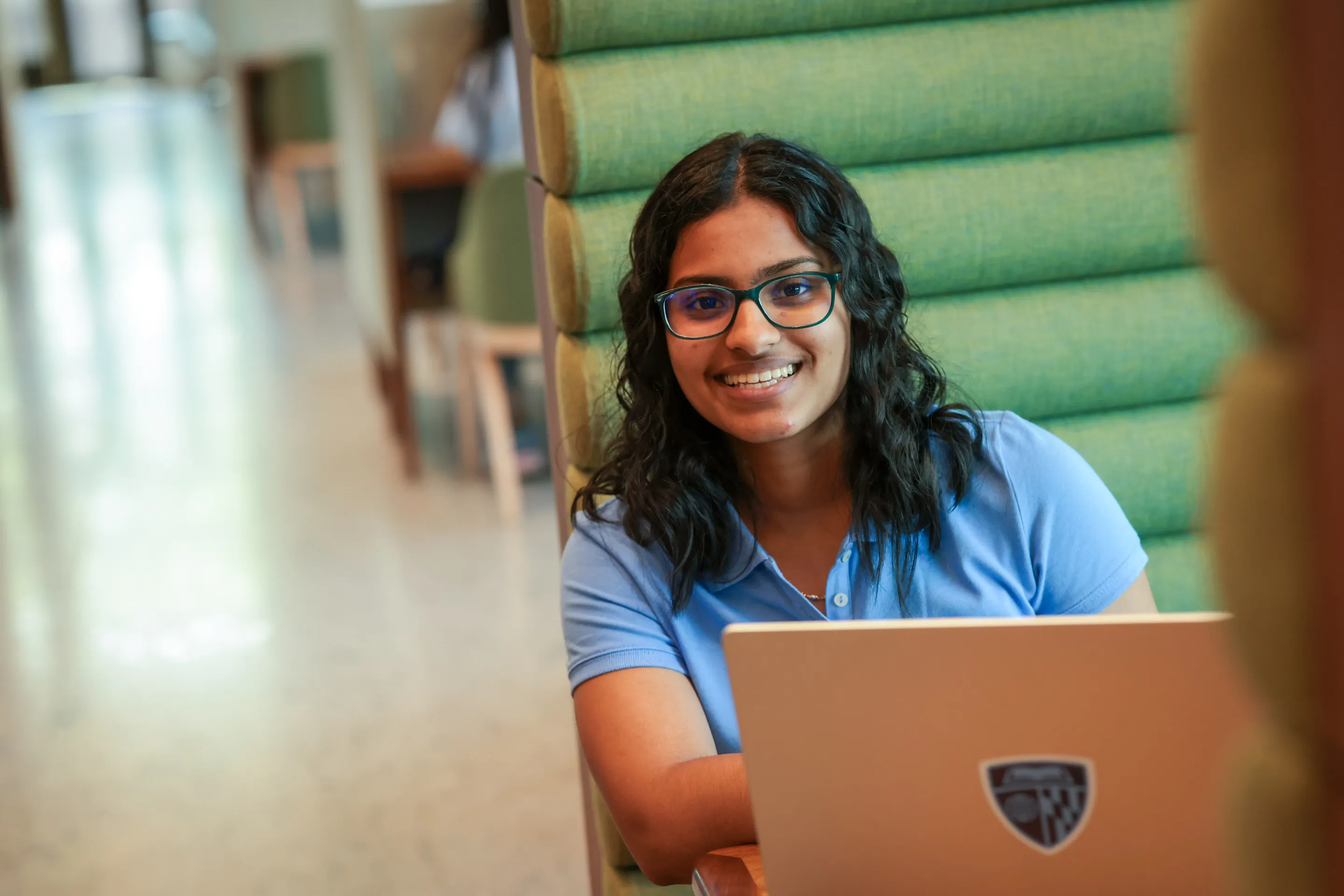 person sitting in booth with laptop, smiling at camera