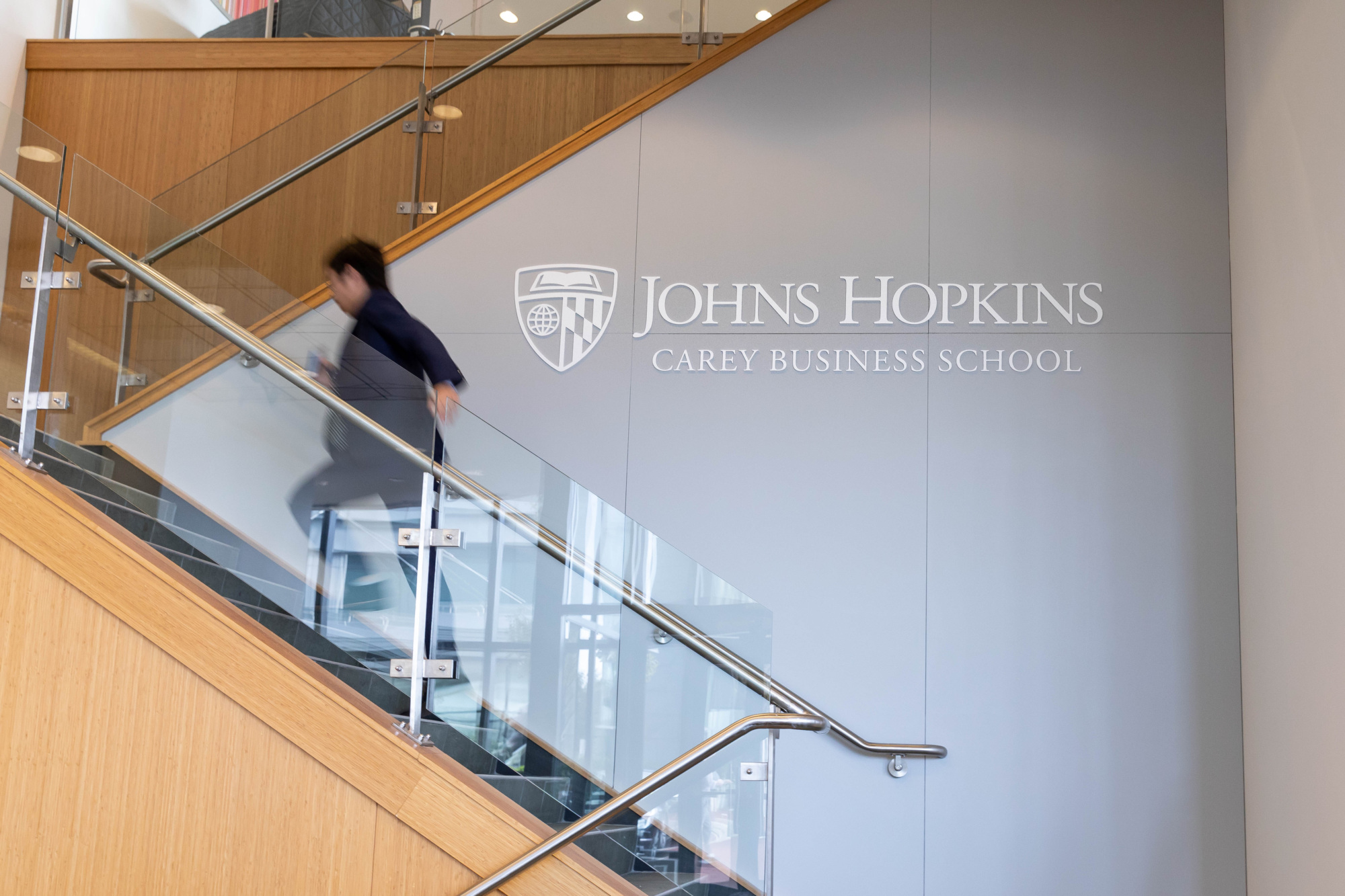 person running up staircase, johns hopkins carey business school logo on wall