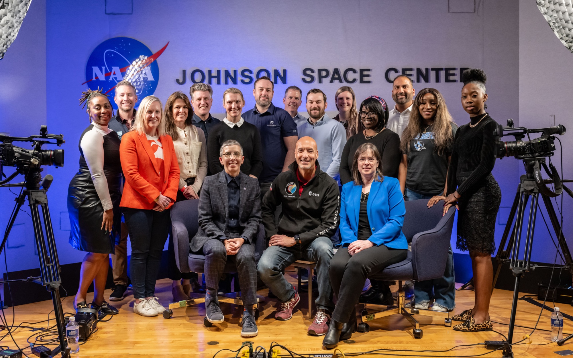 group of people sitting and standing posing for photo in front of johnson space center logo