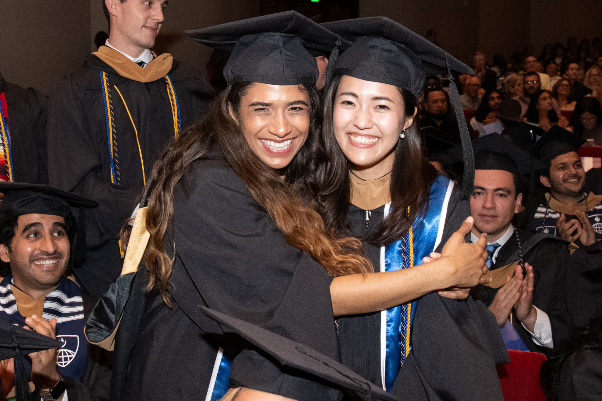 two people posing for photos in graduation regalia. one has hands around the other