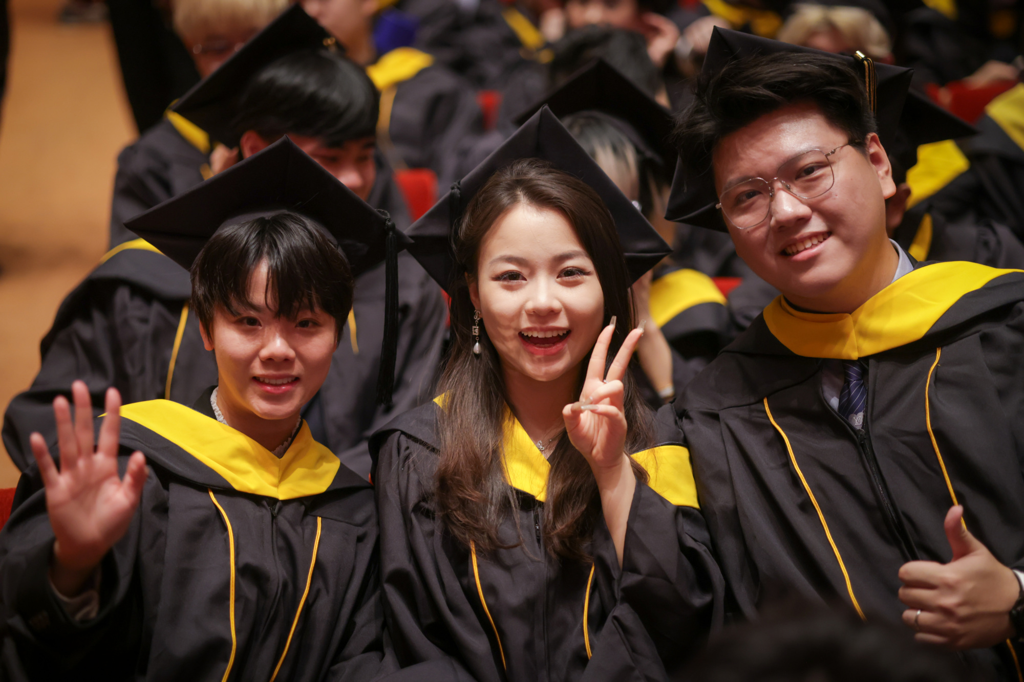 three people posing for photo holding up peace sign in graduation regalia