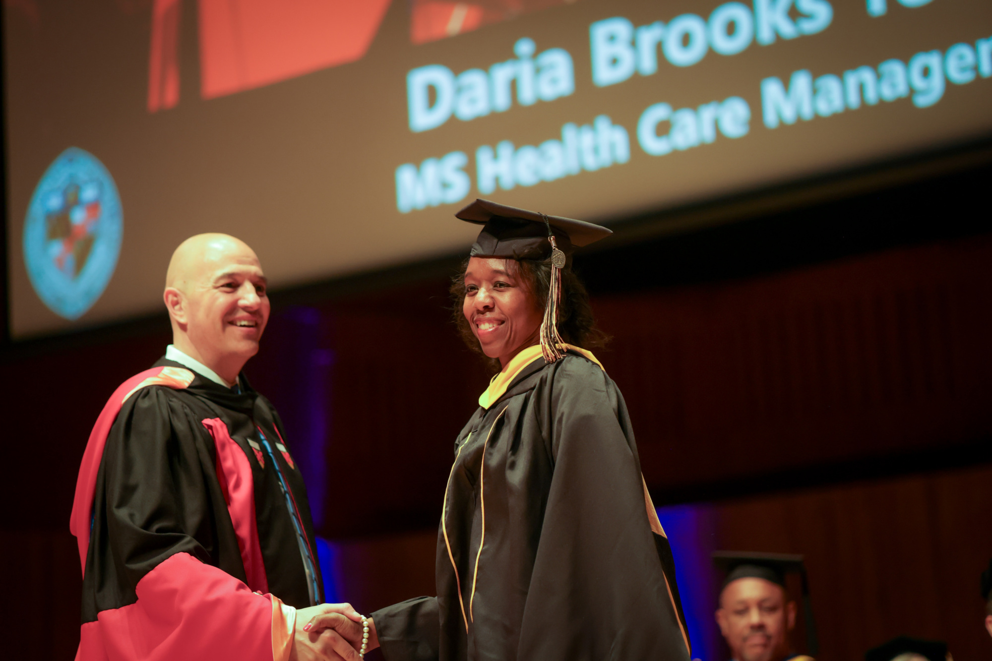 two people shaking hands, smiling on graduation stage