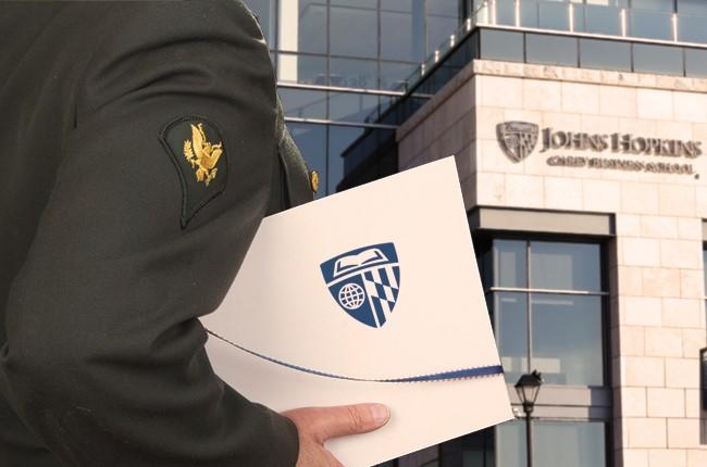 person wearing a military uniform in front of a building holding a folder with carey business school's logo on it