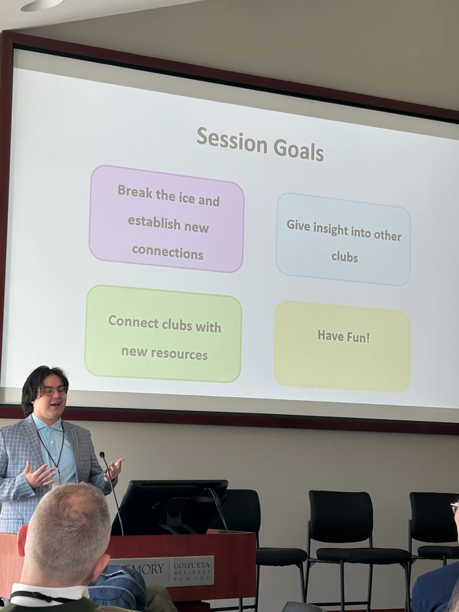 person presenting at front of room with presentation on projector screen in the back