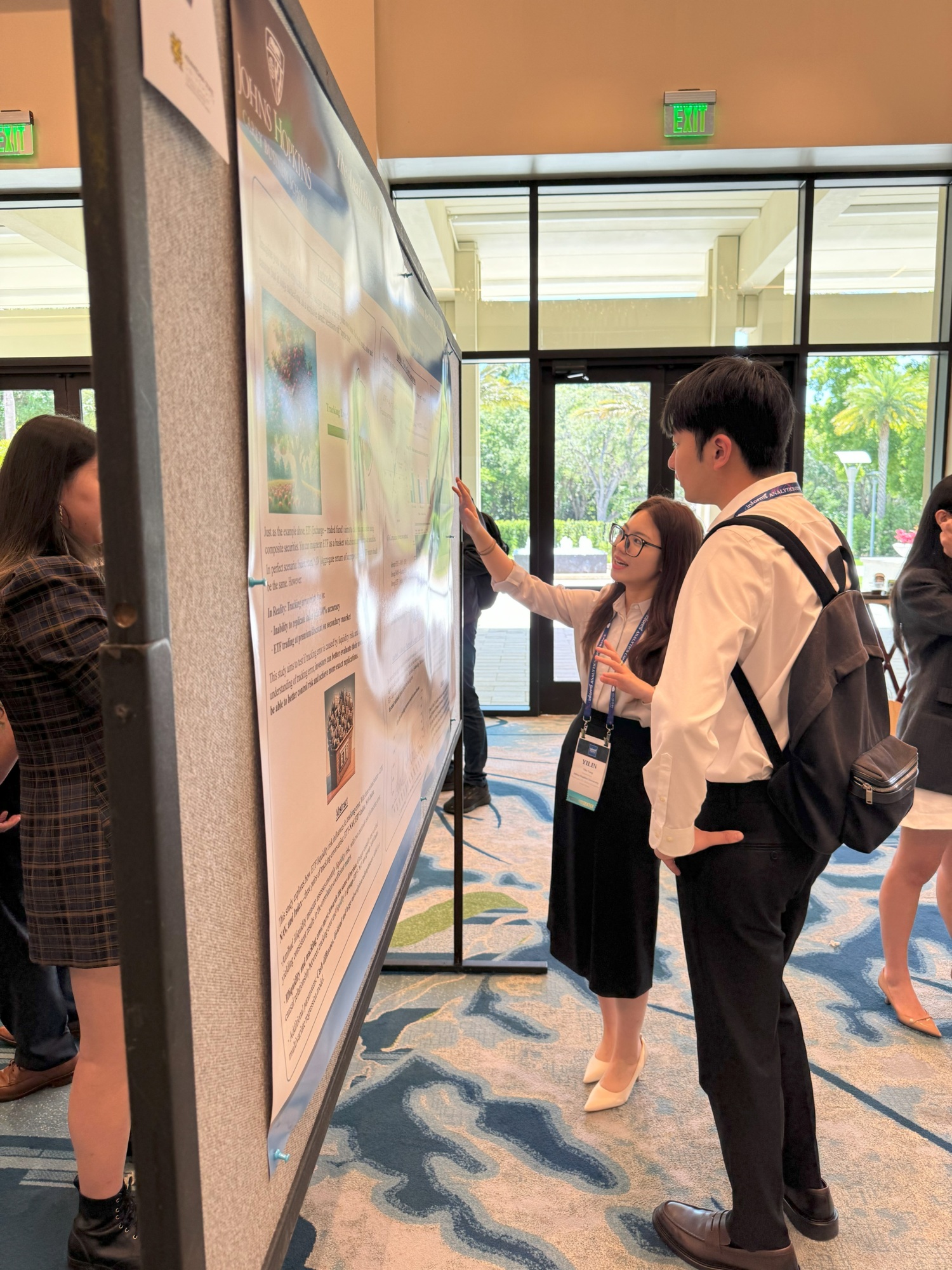 two people standing in front of a poster presentation. one person pointing to poster and other listening