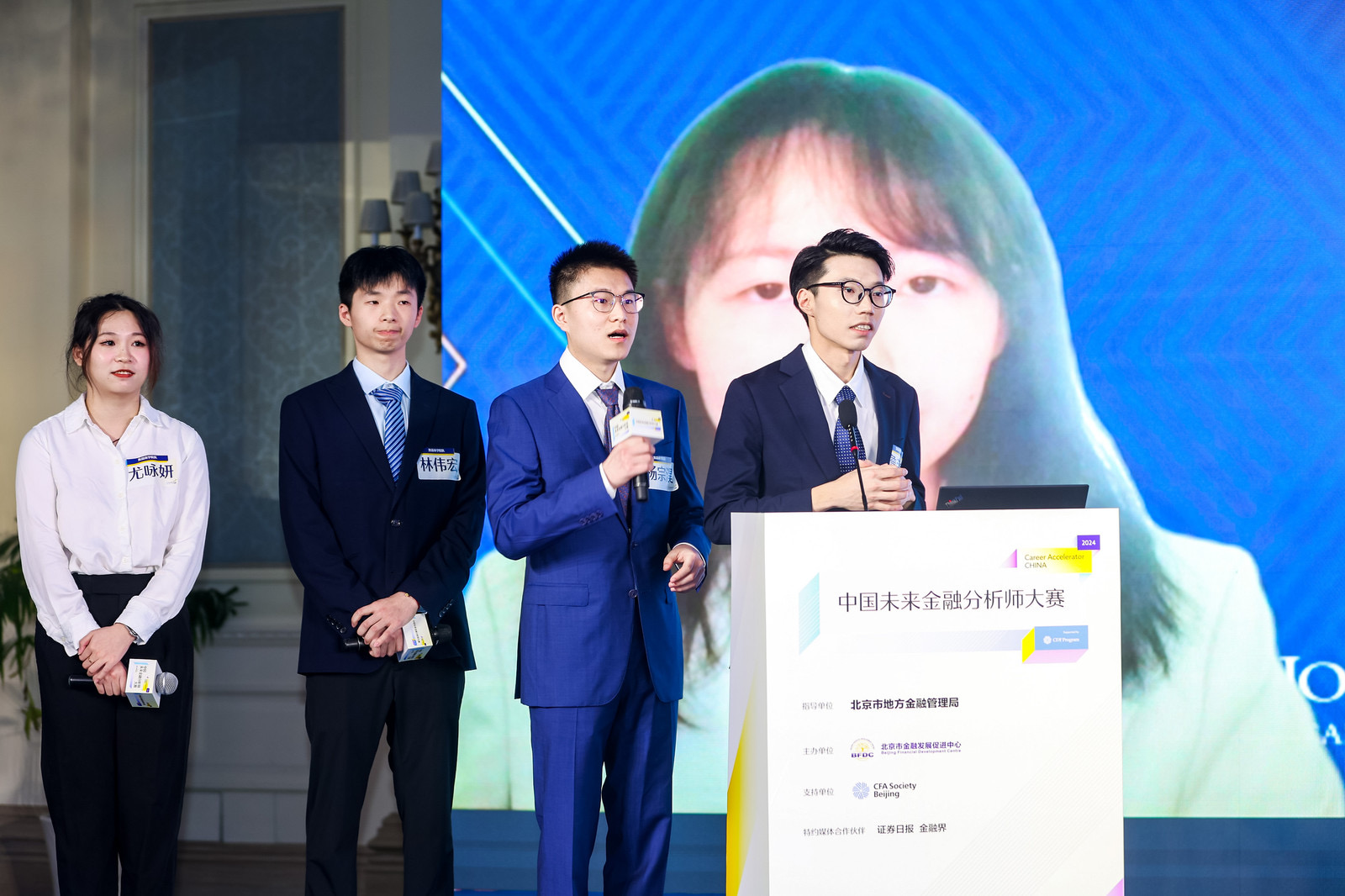 four people on stage with two of them holding microphones presenting in front of a podium