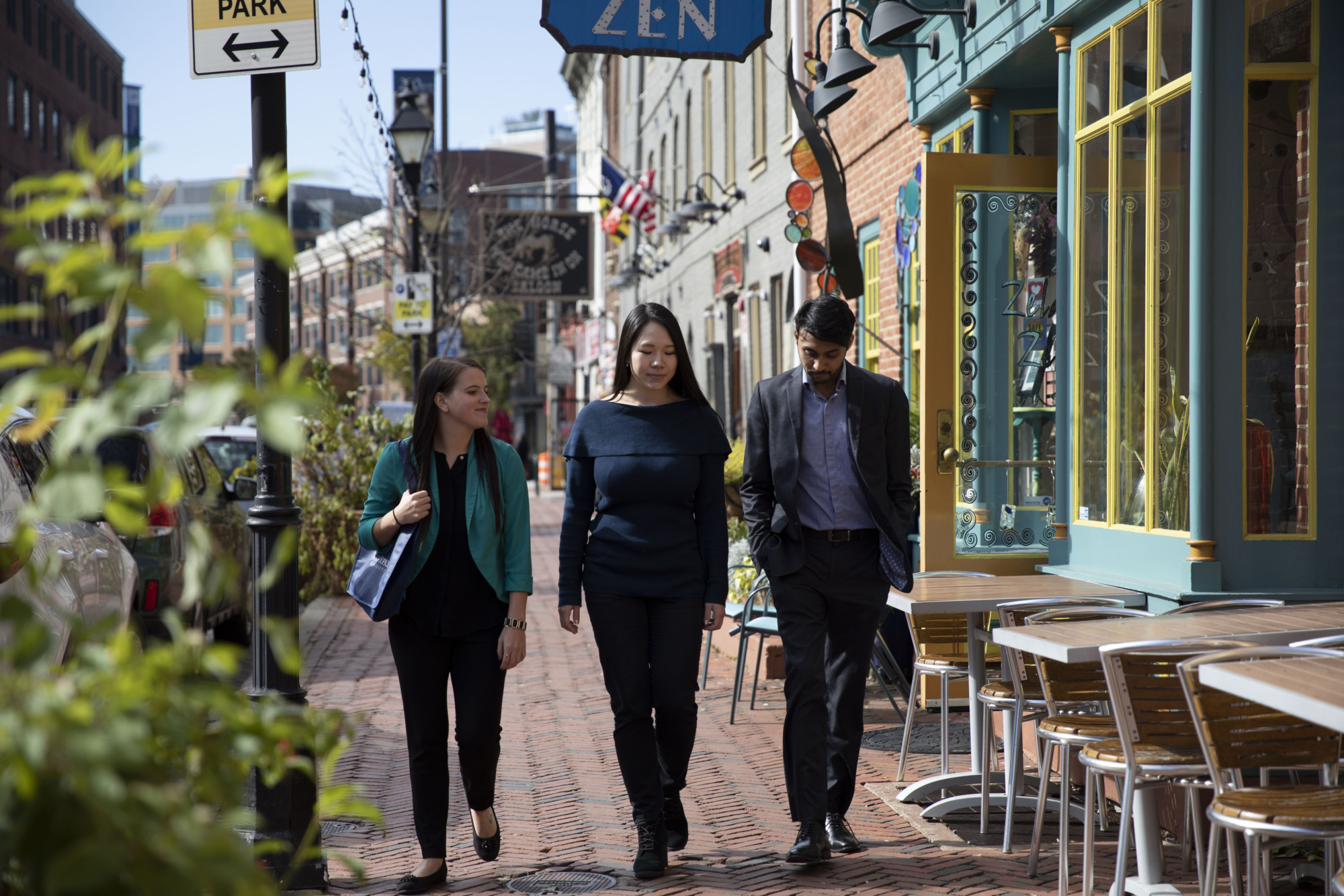 three people walking on a brick street with storefronts in the background