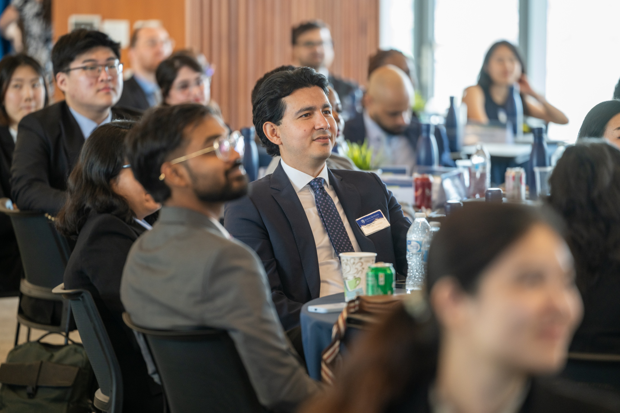 many people sitting at tables, looking ahead. main focus is of two people in suits