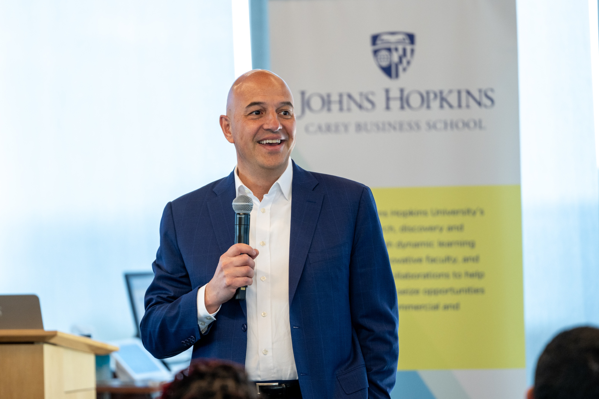 person talking into a microphone with a Johns Hopkins Carey Business School banner in the background