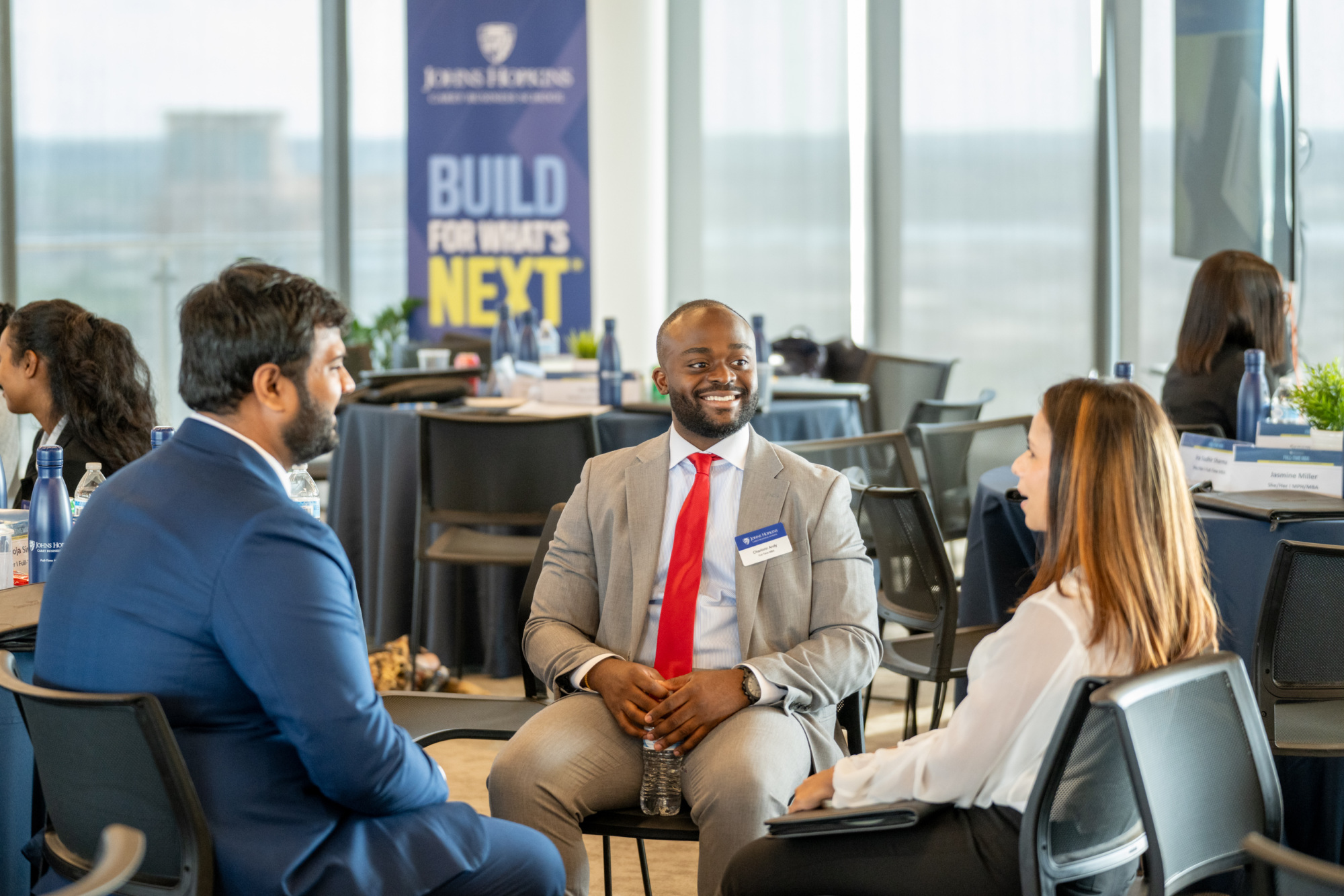 three people in business attire sitting down talking. main focus is of a person smiling at another