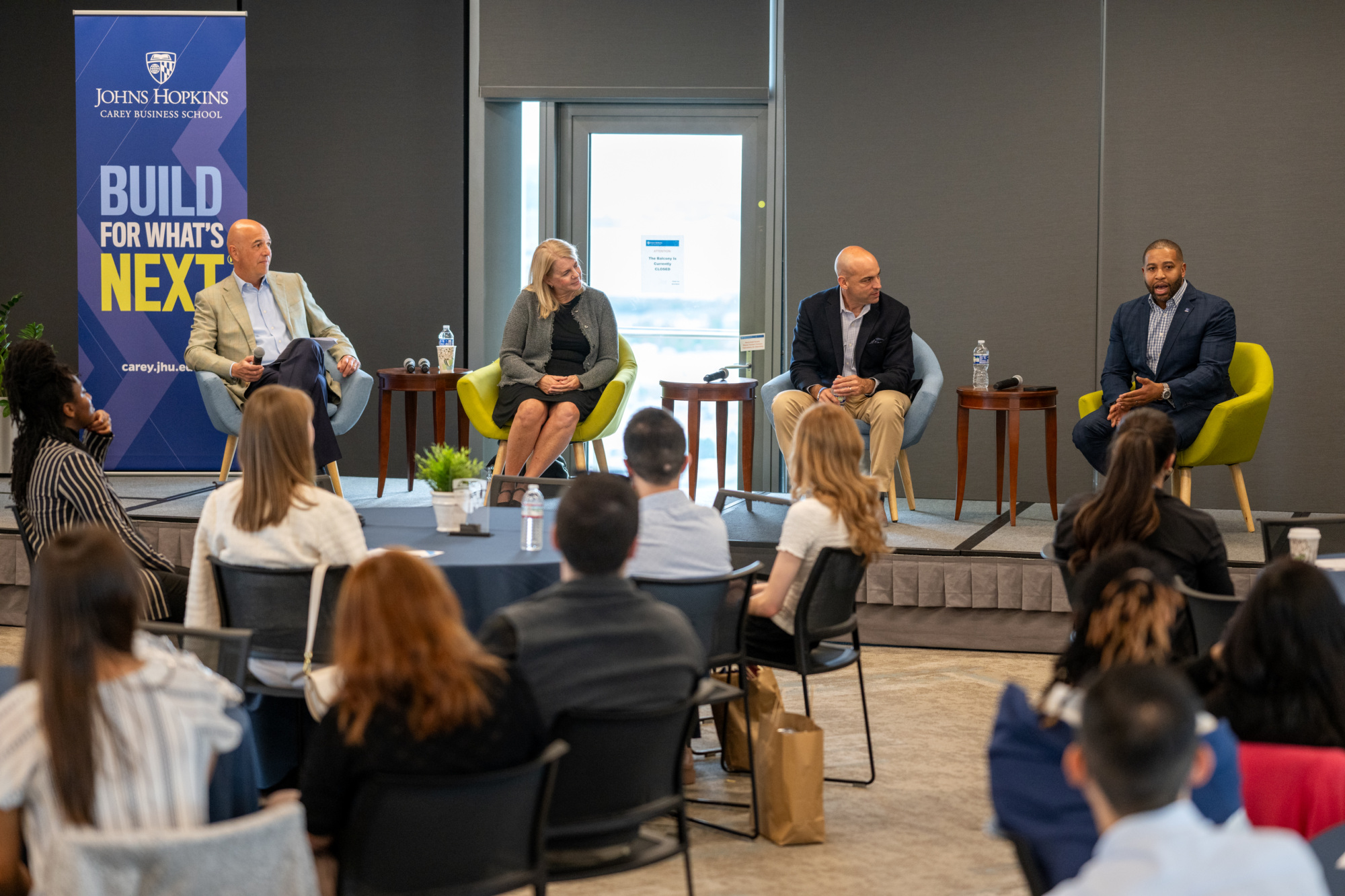 four people sitting on a stage, presenting. people sitting in audience listening