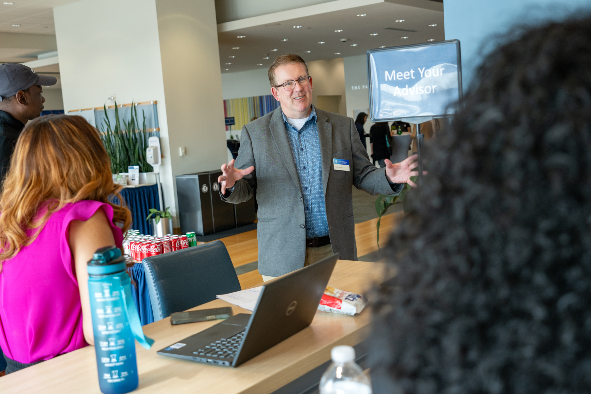 one person standing up speaking to two people sitting at a table. smiling