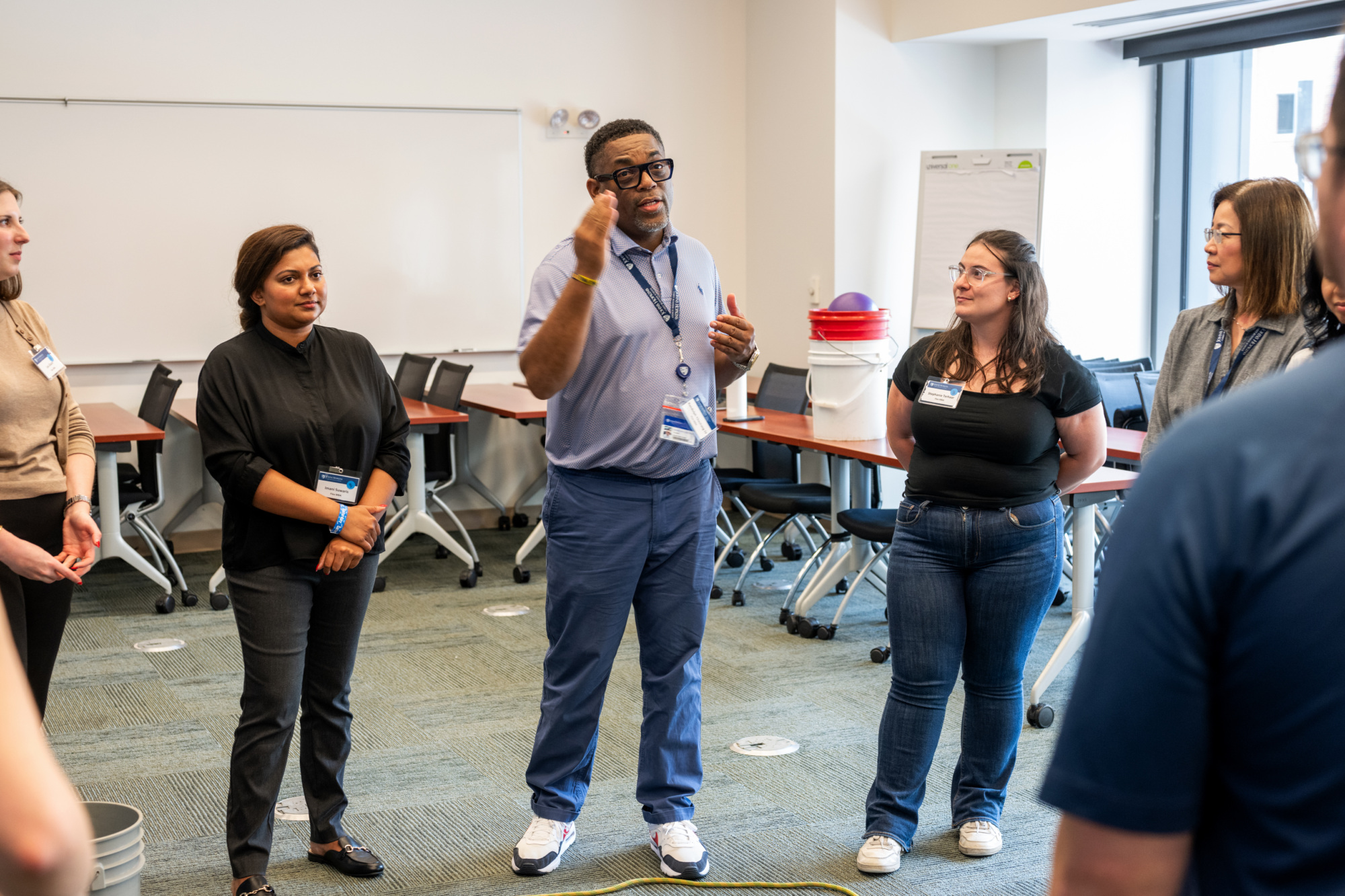 six people standing in a circle listening to one person speak, they are using their hands while talking