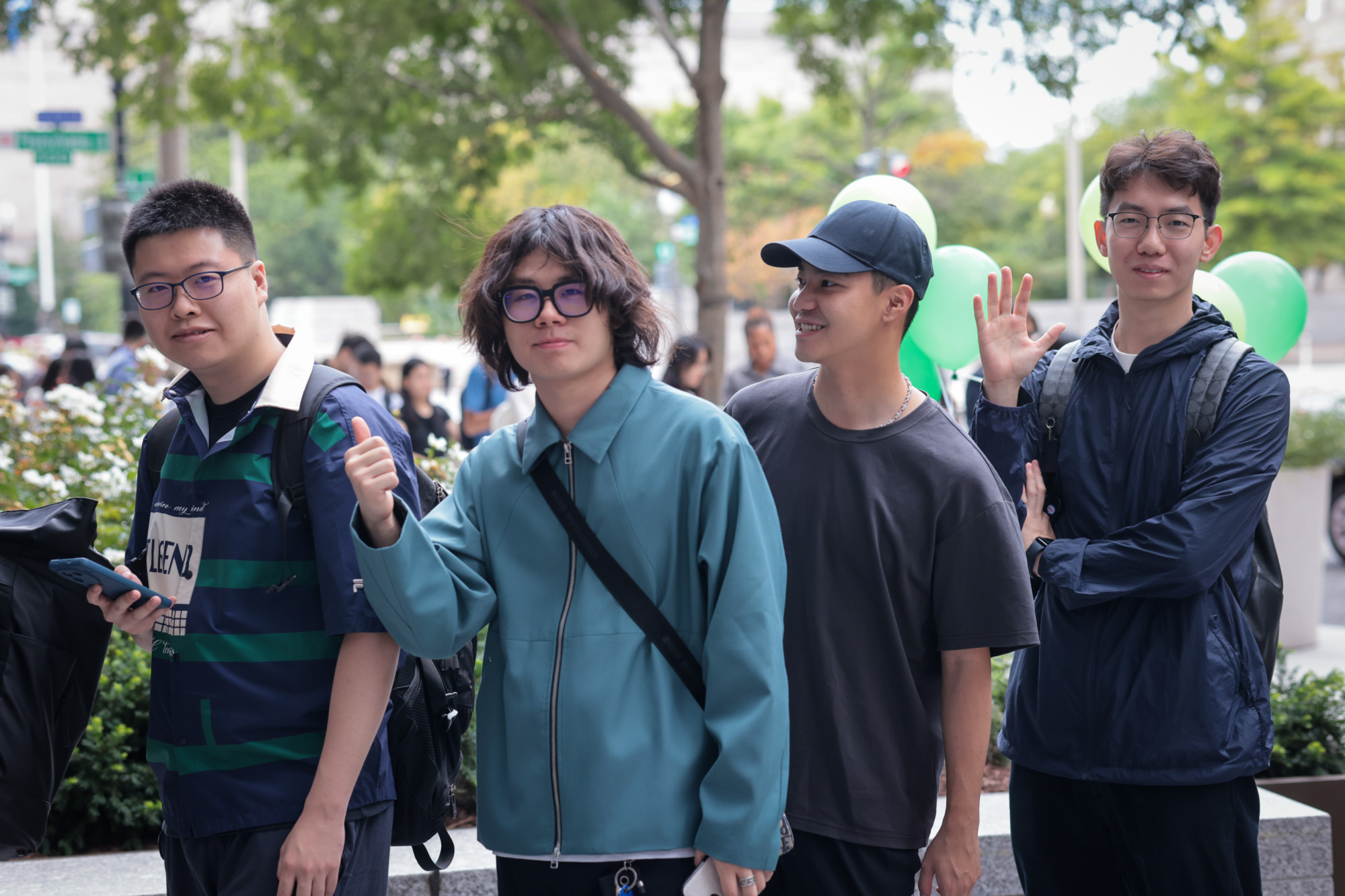 four people standing outside posing for the camera. main subject has a thumbs up