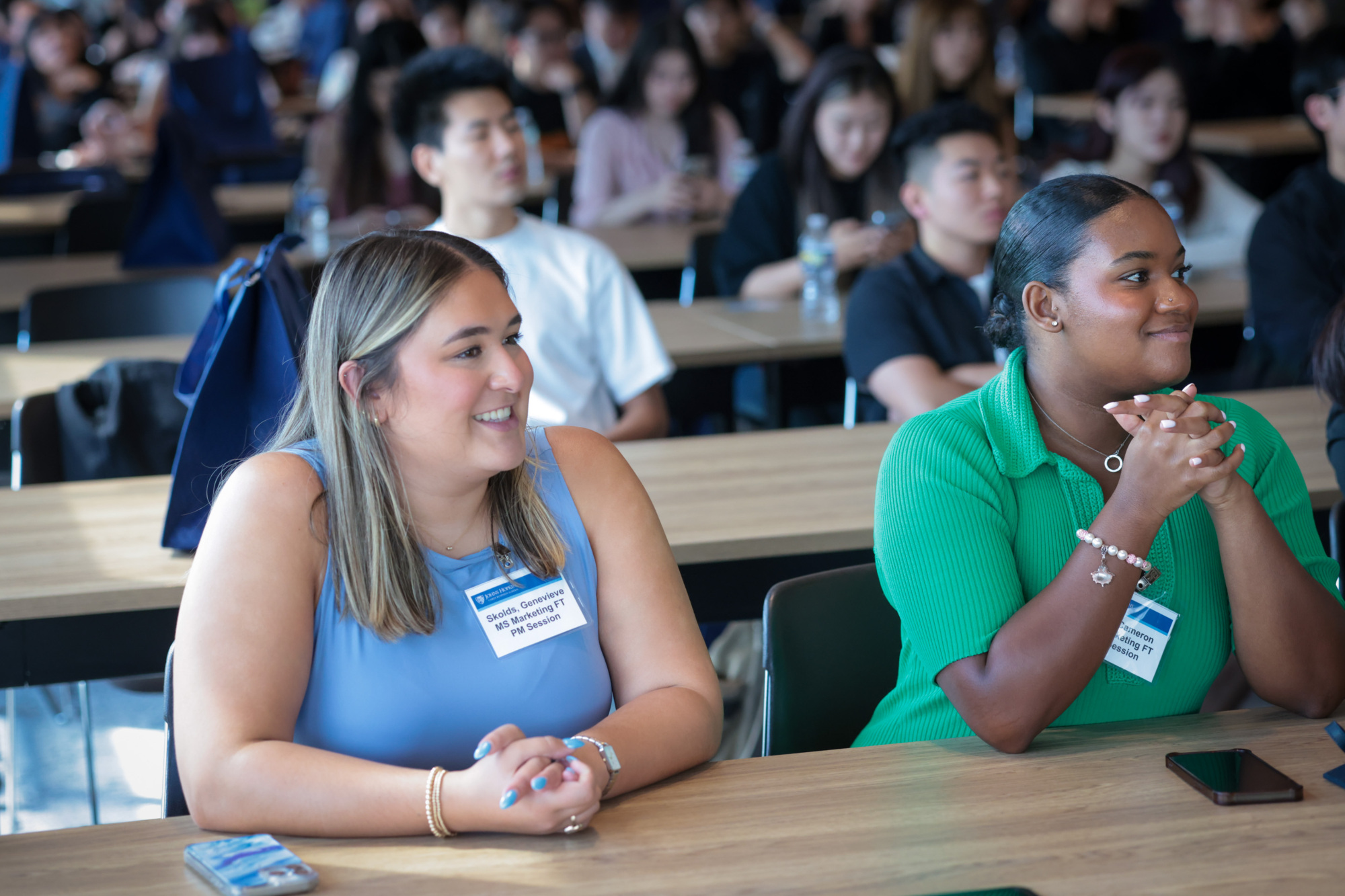 people sitting at desks with the main focus of two people in the front. both smiling