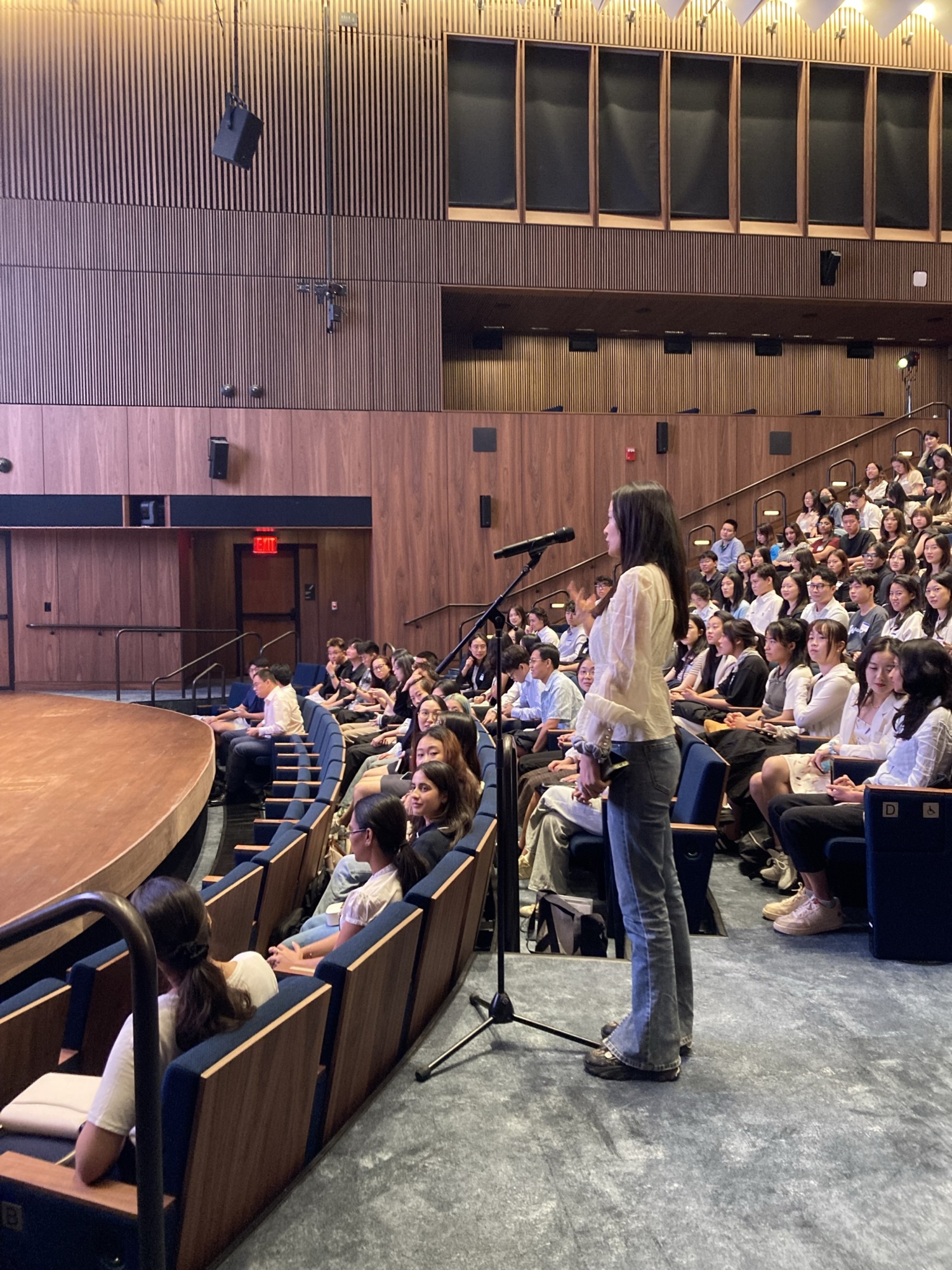 person standing up in an audience filled with people talking into a microphone