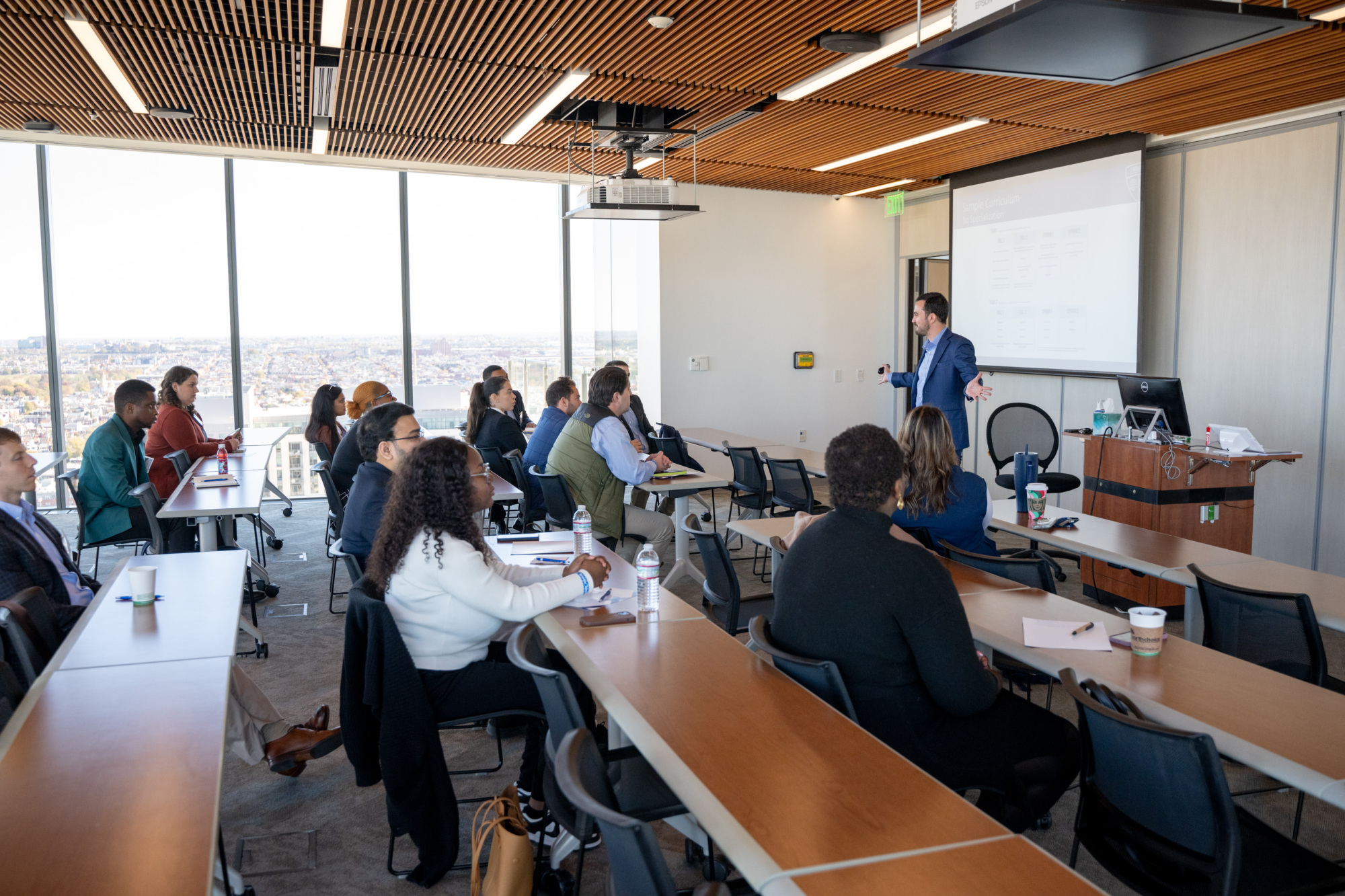 person speaking to a room full of people all sitting at desks