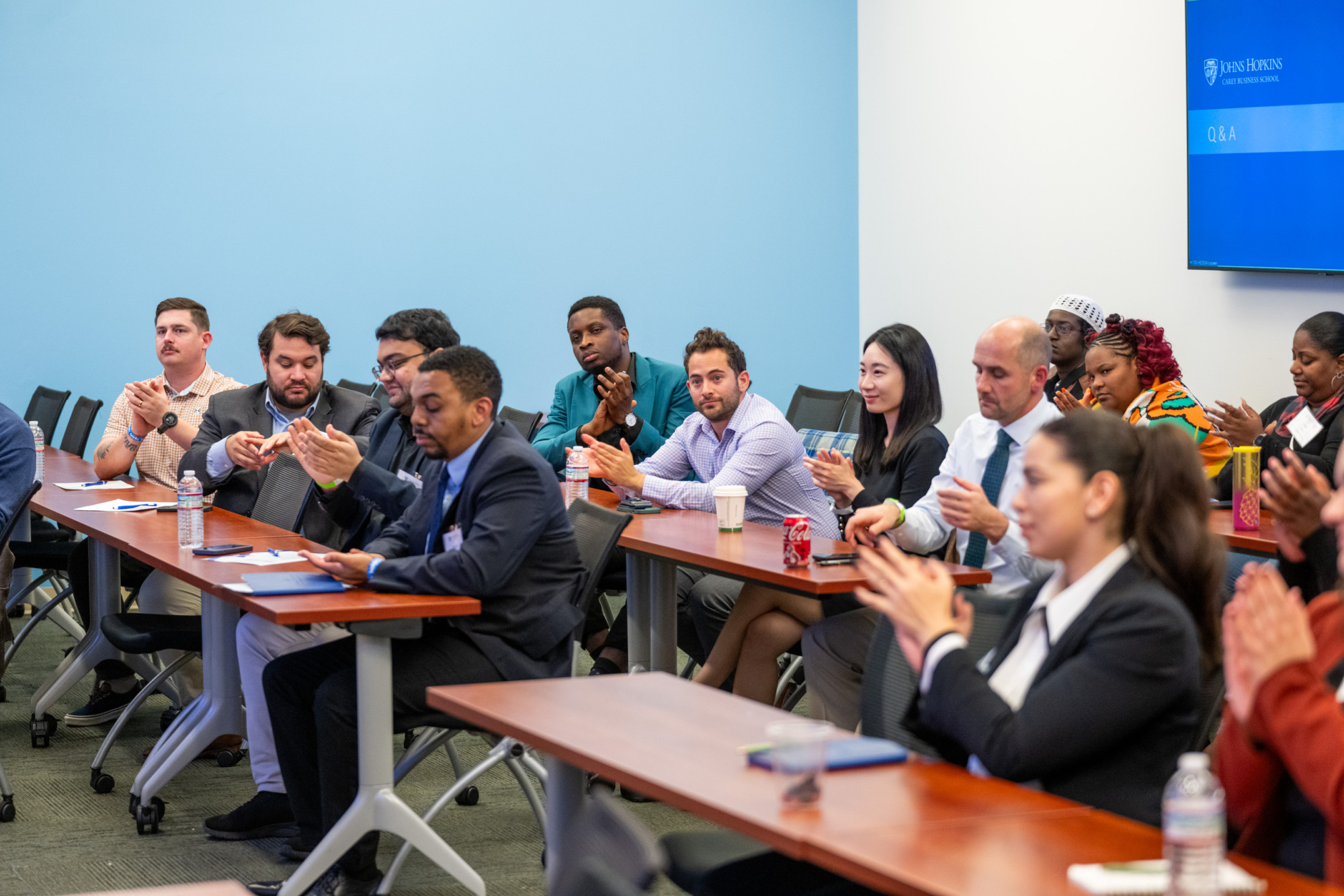 people sitting at long desks in a classroom clapping