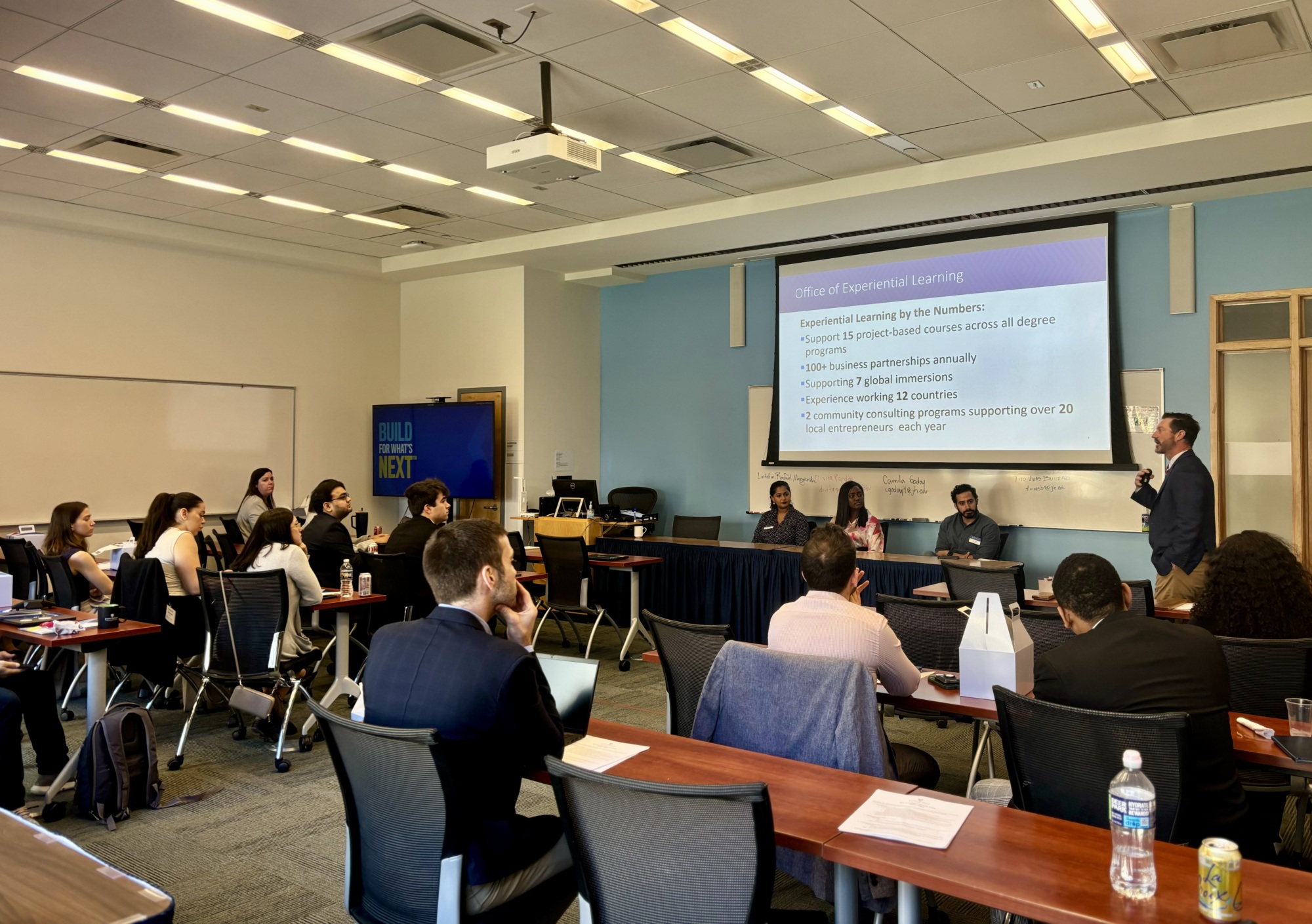 people sitting in a classroom watching someone present