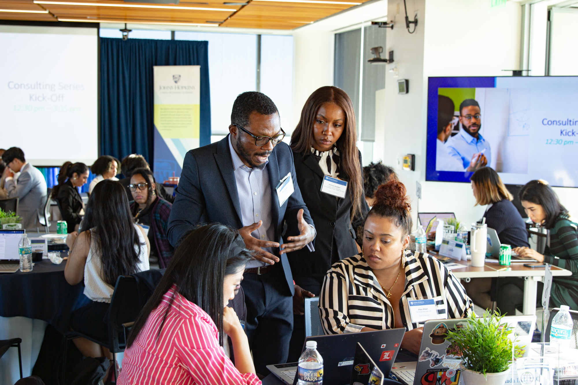 two people standing up talking to a group of people at a table